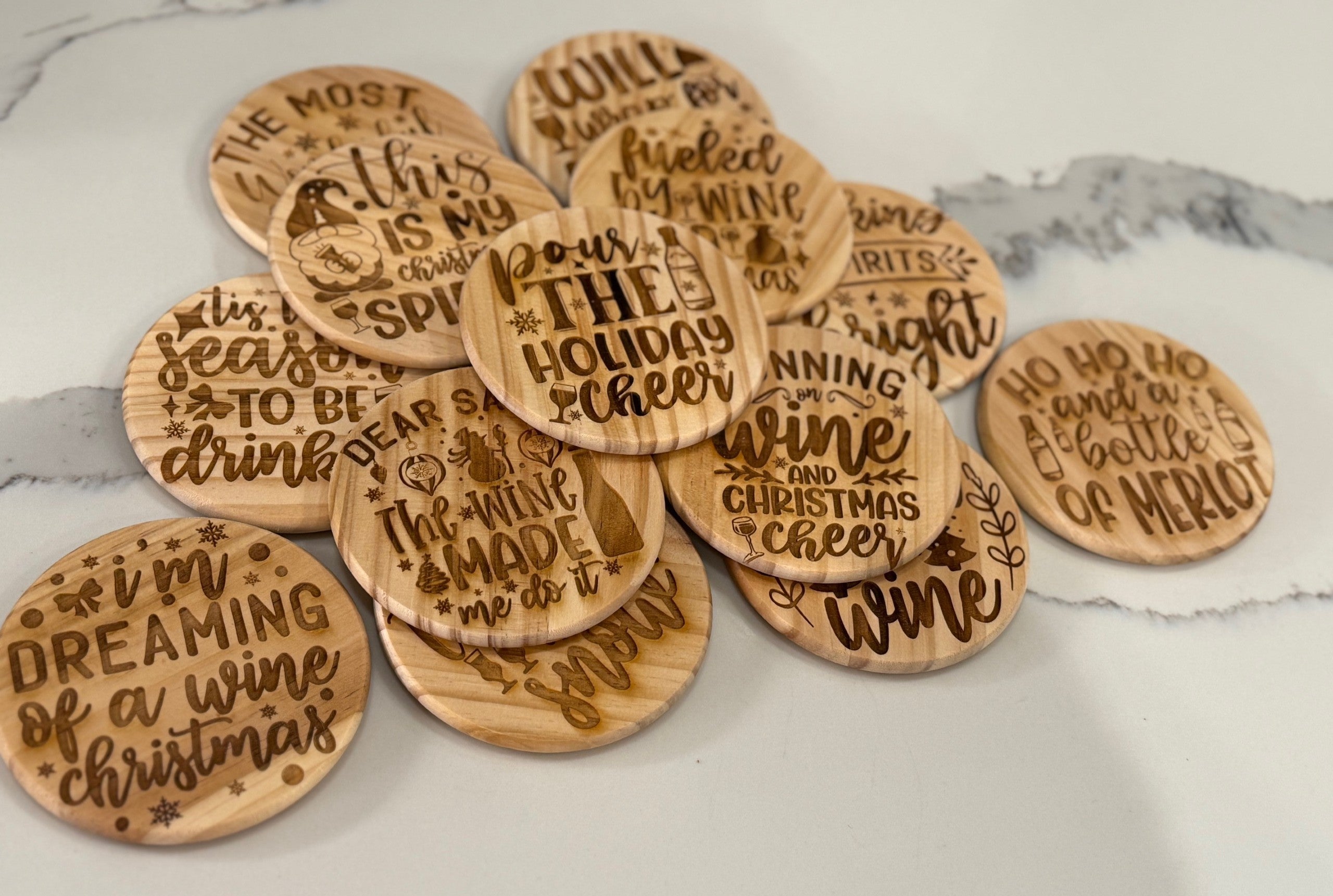 The Funny Wine Sayings: Set of 4 Round Wooden Coasters features engraved holiday and wine sayings, each with a unique festive and humorous design on a white marble surface with subtle gray veining.