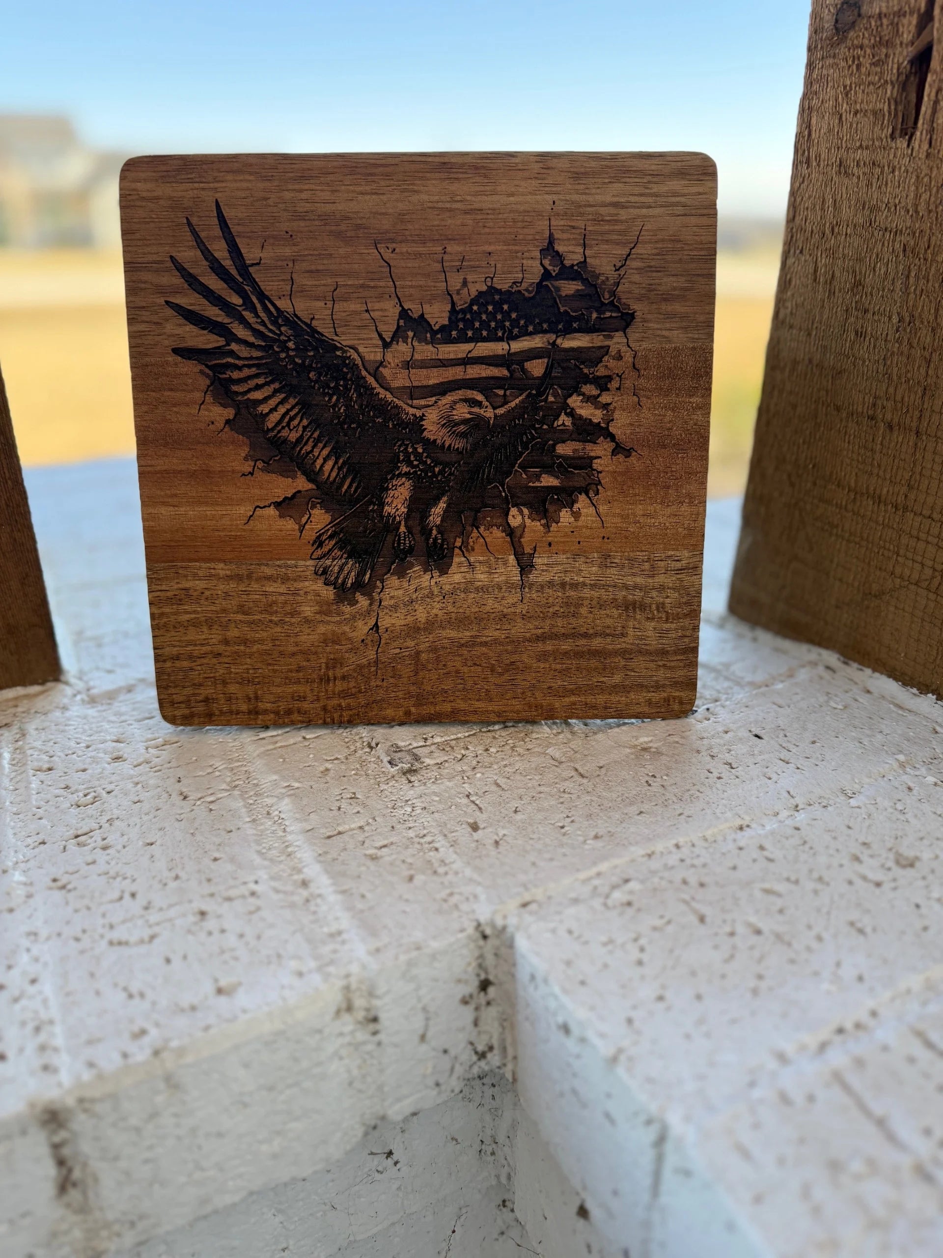 This Patriotic 3D Eagle Flag engraved Acacia Wood Cutting Board features a detailed eagle with carved wings and a stylized American flag. Crafted from acacia wood, it rests on a white brick surface against a softly blurred background.