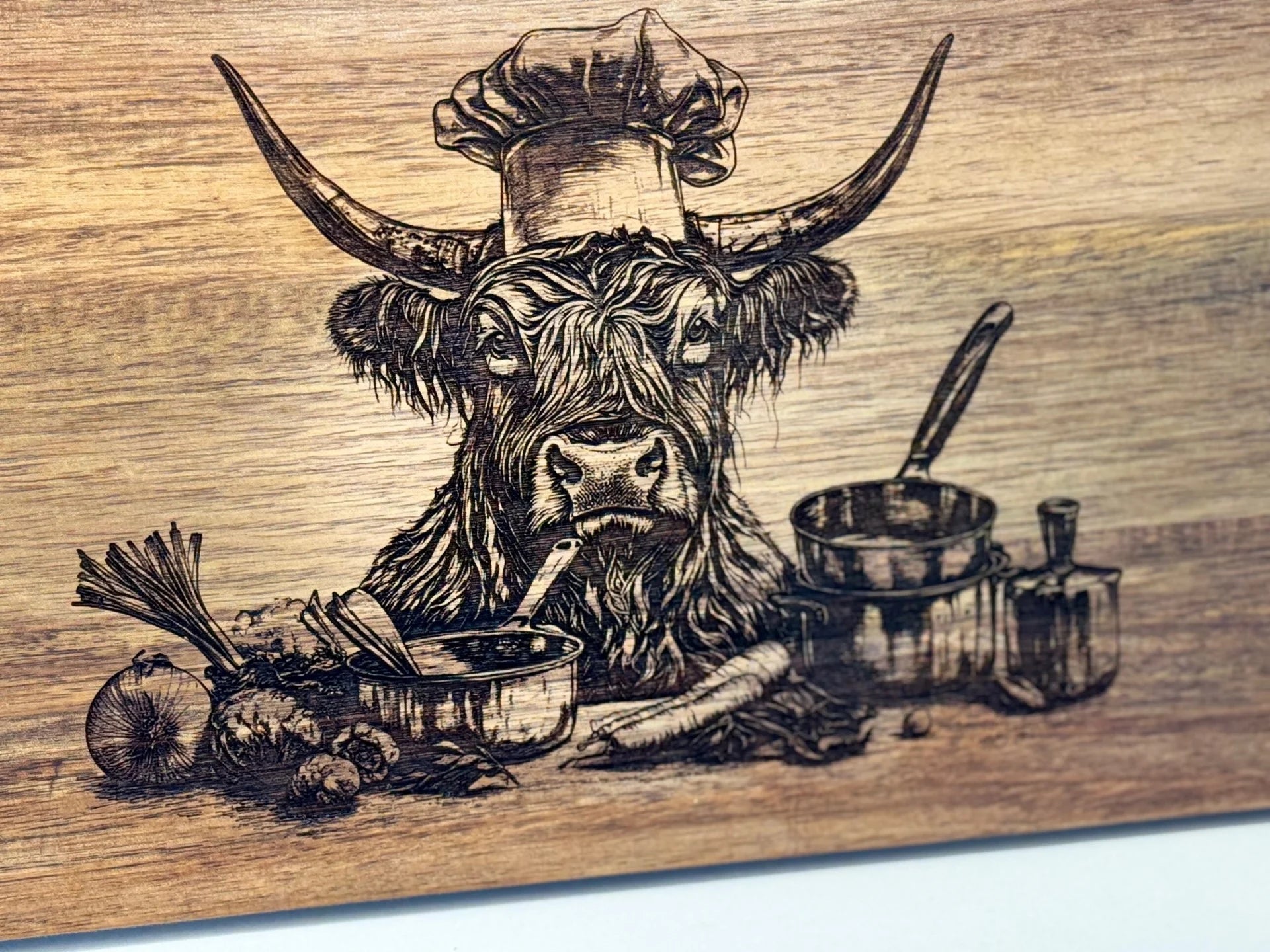 This BBQ Grill Chart engraved Acacia Wood Cutting Board features a Highland cow in a chefs hat surrounded by cooking elements, merging rustic charm with culinary flair—a must-have for BBQ enthusiasts.