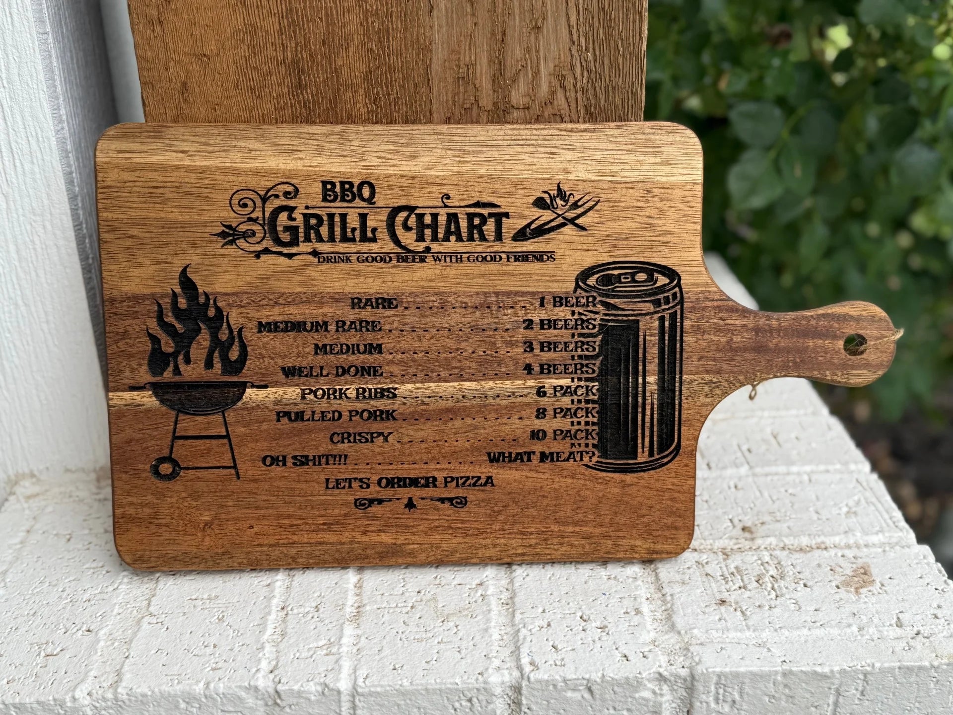 The BBQ Grill Chart engraved Acacia Wood Cutting Board features a funny meat doneness and beer pairing guide, playful grill and beer can art, and ends with “OH SHIT!! LETS ORDER PIZZA.”.