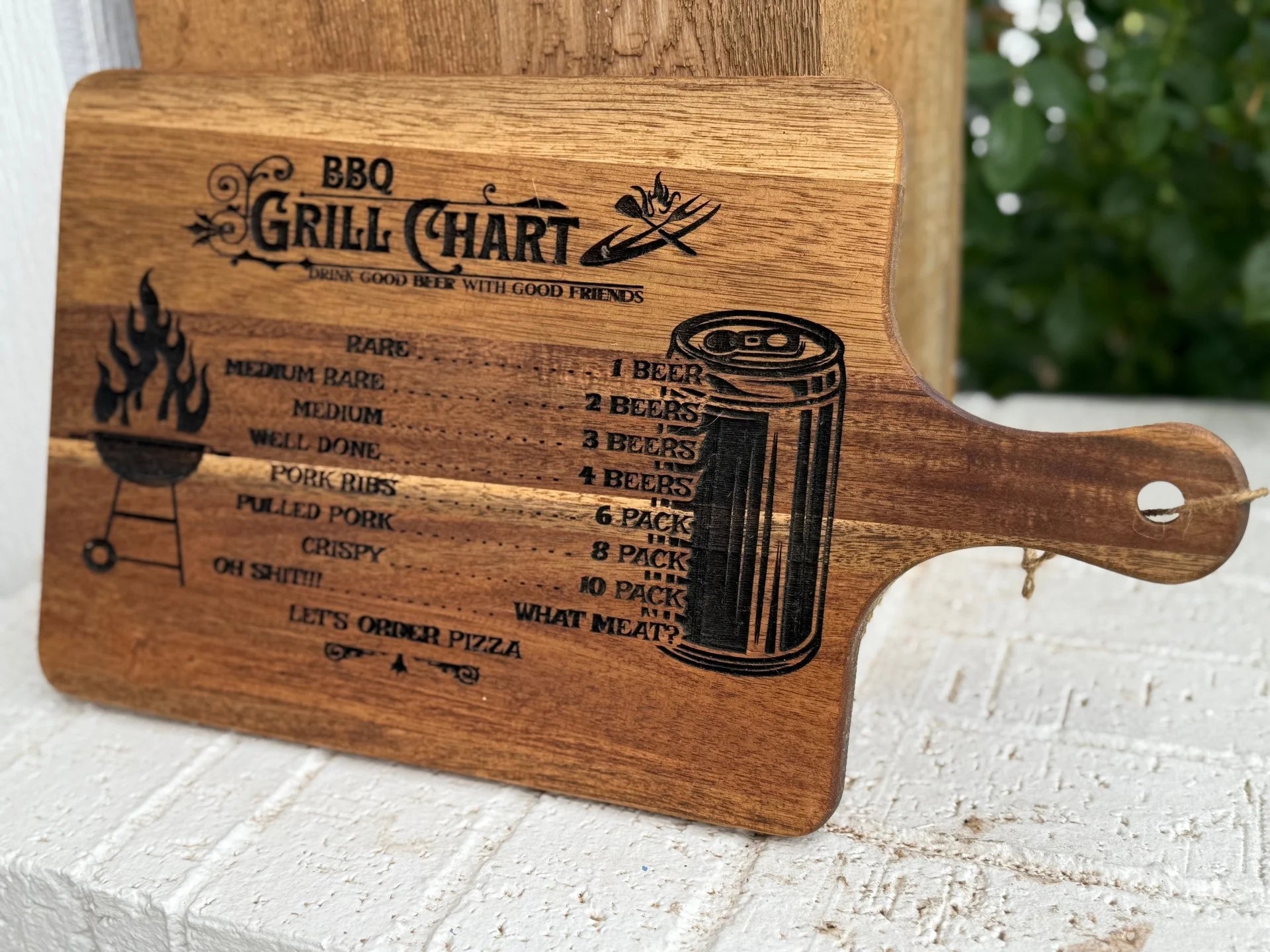 The BBQ Grill Chart engraved Acacia Wood Cutting Board shows meat doneness paired with beer amounts, includes a grilled meat illustration, and features Lets order pizza at the bottom.
