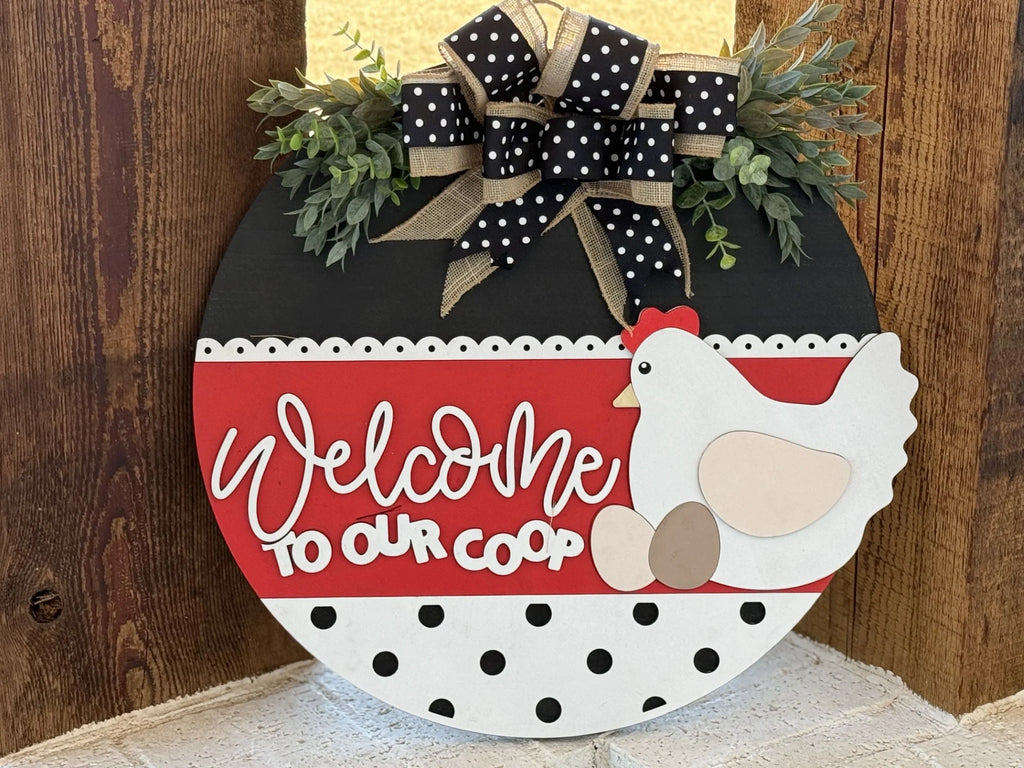 The If Were Not Home Check the Rink door wreath features a round wooden design with Welcome to Our Coop in white cursive on a red background, black polka dots on white below, and a hen with two eggs. A black and white polka dot bow with greenery tops it off, ideal for home decor lovers.