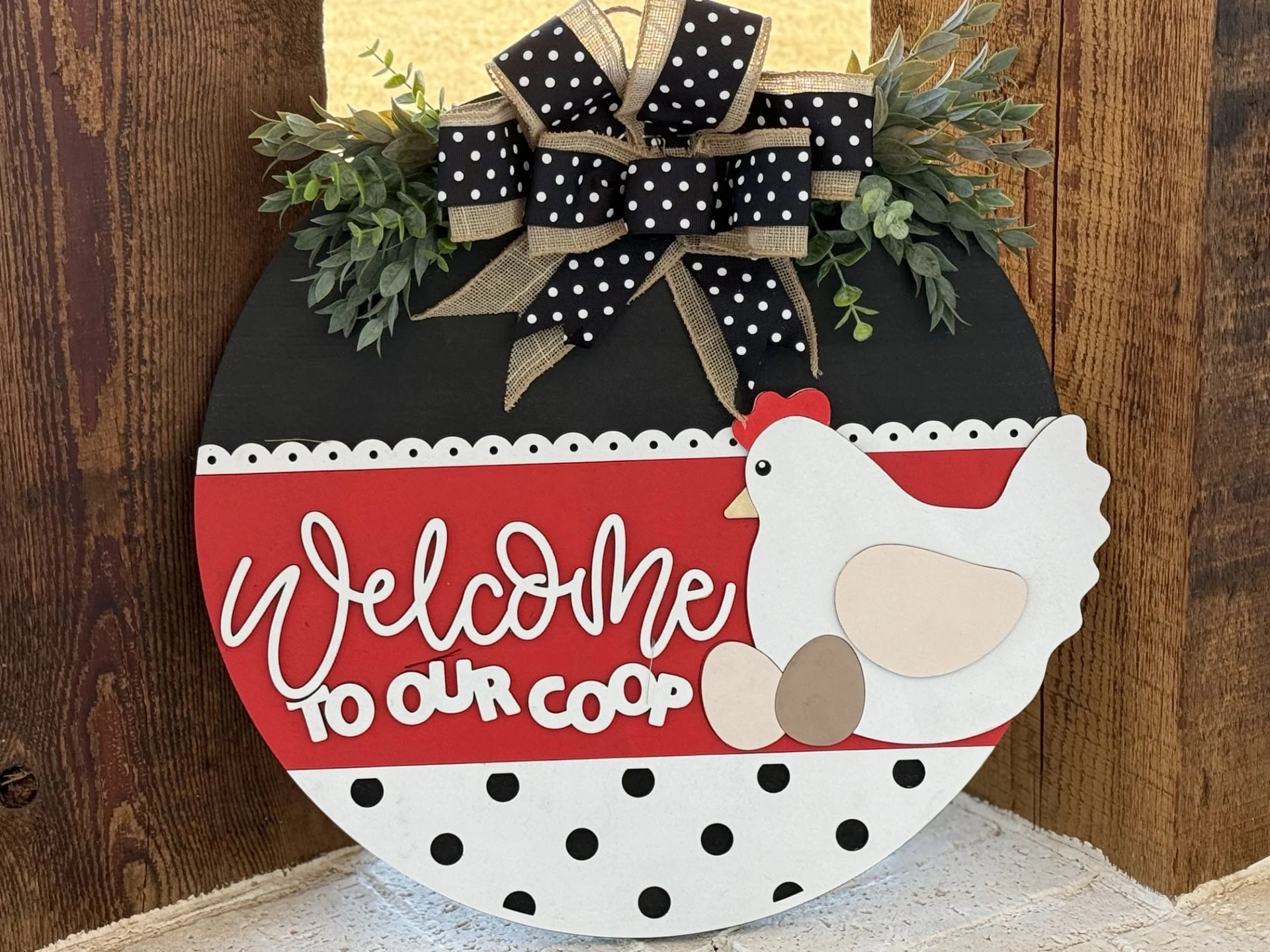 The If Were Not Home Check the Rink Door Sign, Door Wreath showcases a round wooden design with a red and black polka dot background, featuring a white chicken, two eggs, Welcome to Our Coop text, topped with a decorative black bow with white dots and greenery—ideal for any wooden door.