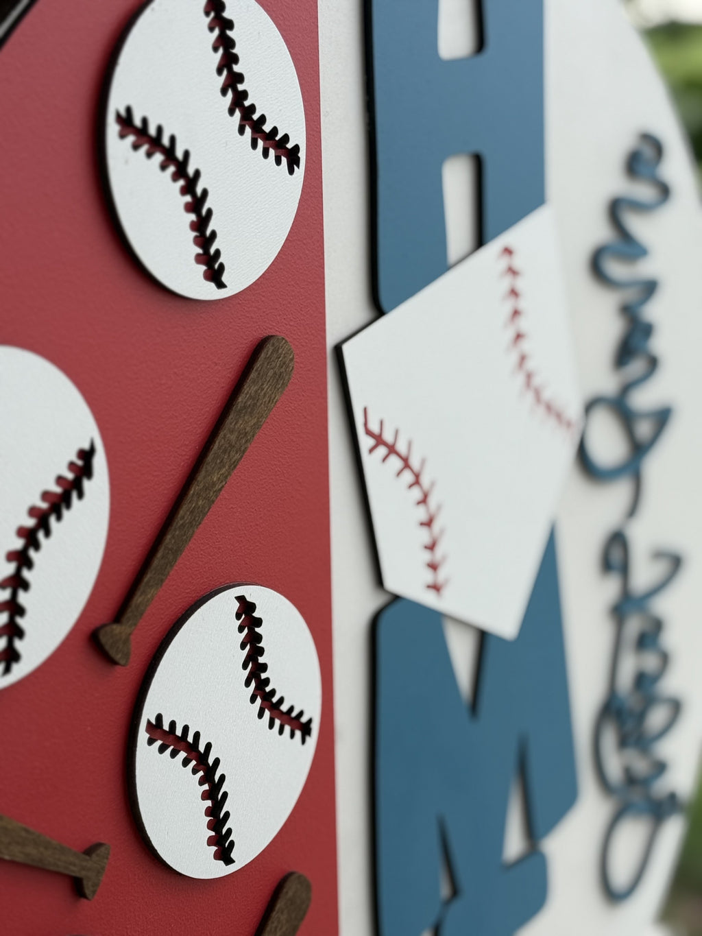 A close-up of a decorative sign featuring cutouts of baseballs, bats, and letters in red, white, blue, and brown colors, with a baseball theme.