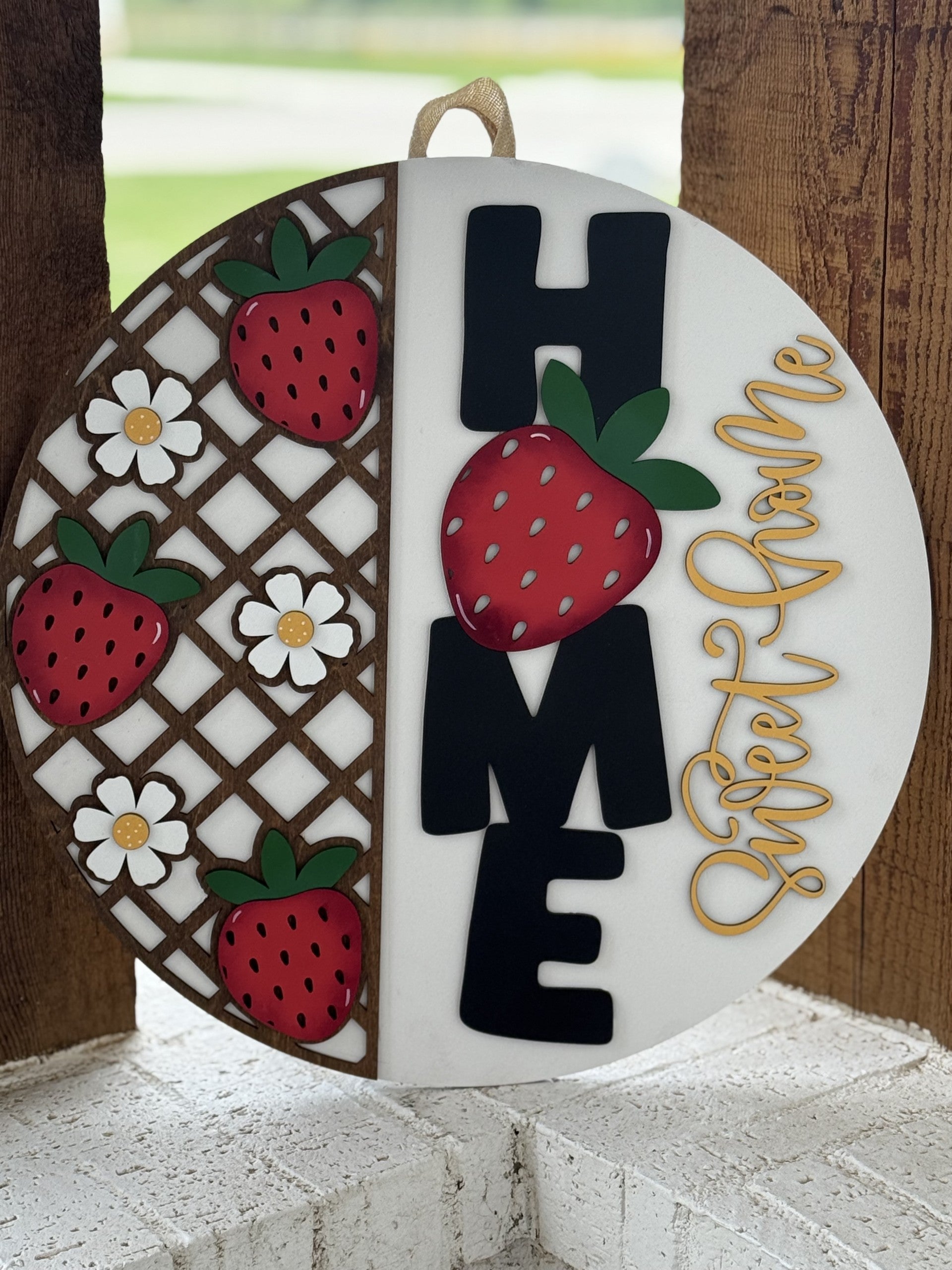 A round decorative sign features strawberries, white flowers, the word HOME in bold black letters with a strawberry for the O, and the phrase Sweet Home in cursive yellow on a white background.