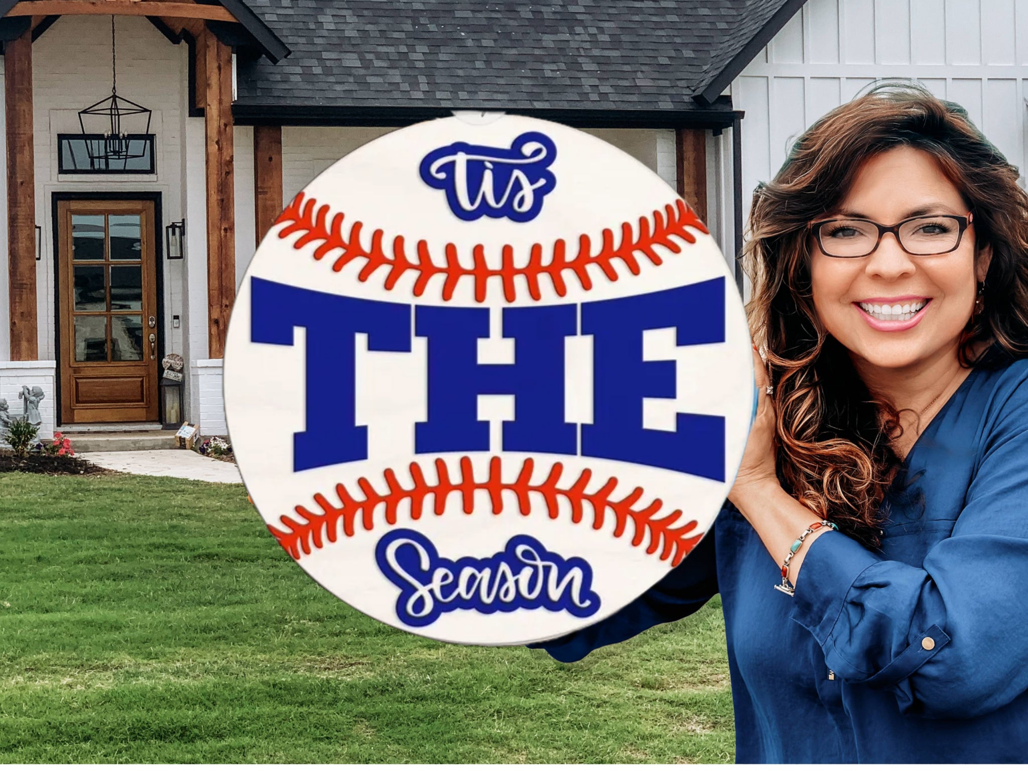 A smiling woman in glasses and a blue shirt stands outside a house, holding a large baseball-shaped sign that reads Its THE Season in decorative lettering.