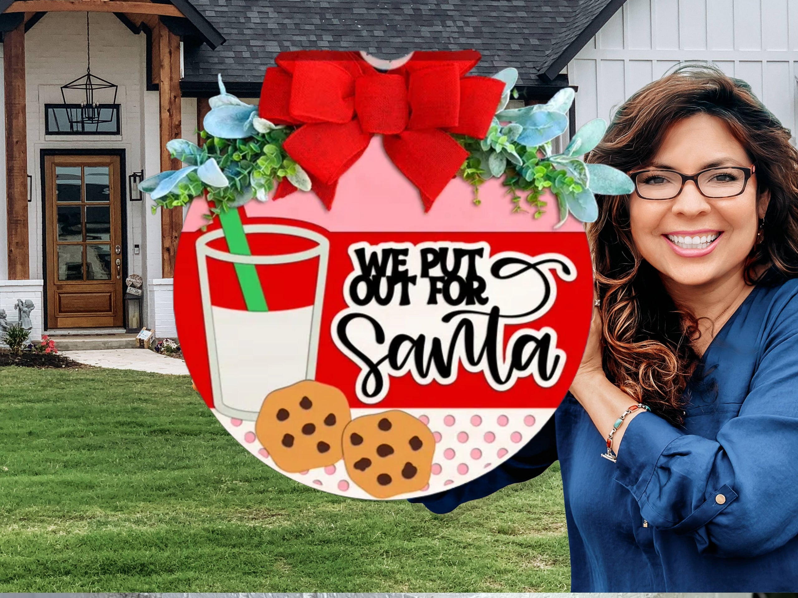A smiling woman with long brown hair and glasses holds a round holiday sign with a red bow. The sign features milk, cookies, and text that reads “We put out for Santa.” A modern house exterior is in the background.