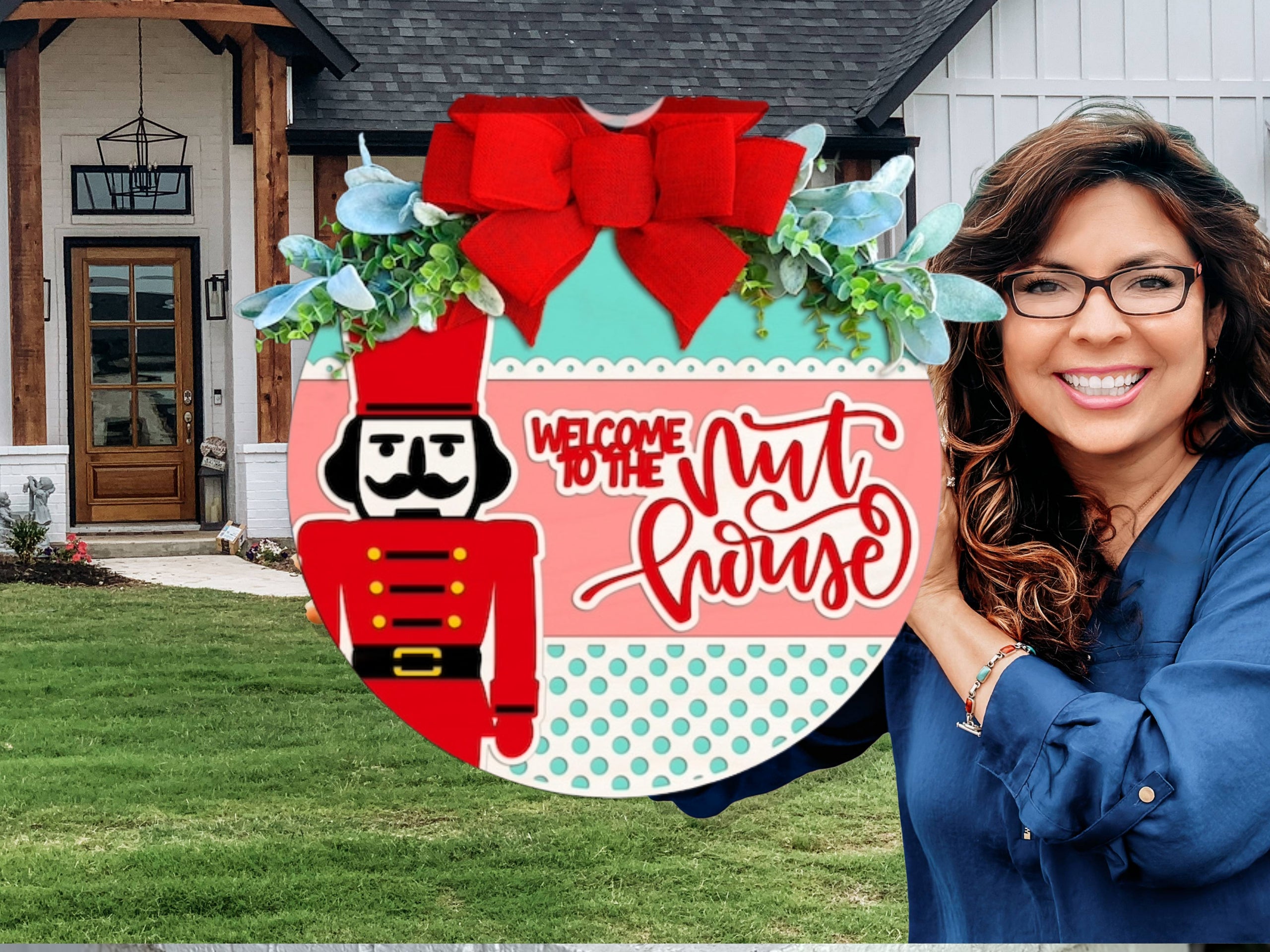 A smiling woman with long brown hair and glasses holds a round festive sign featuring a nutcracker, red bow, greenery, and the words Welcome to the Nut House in front of a modern house.