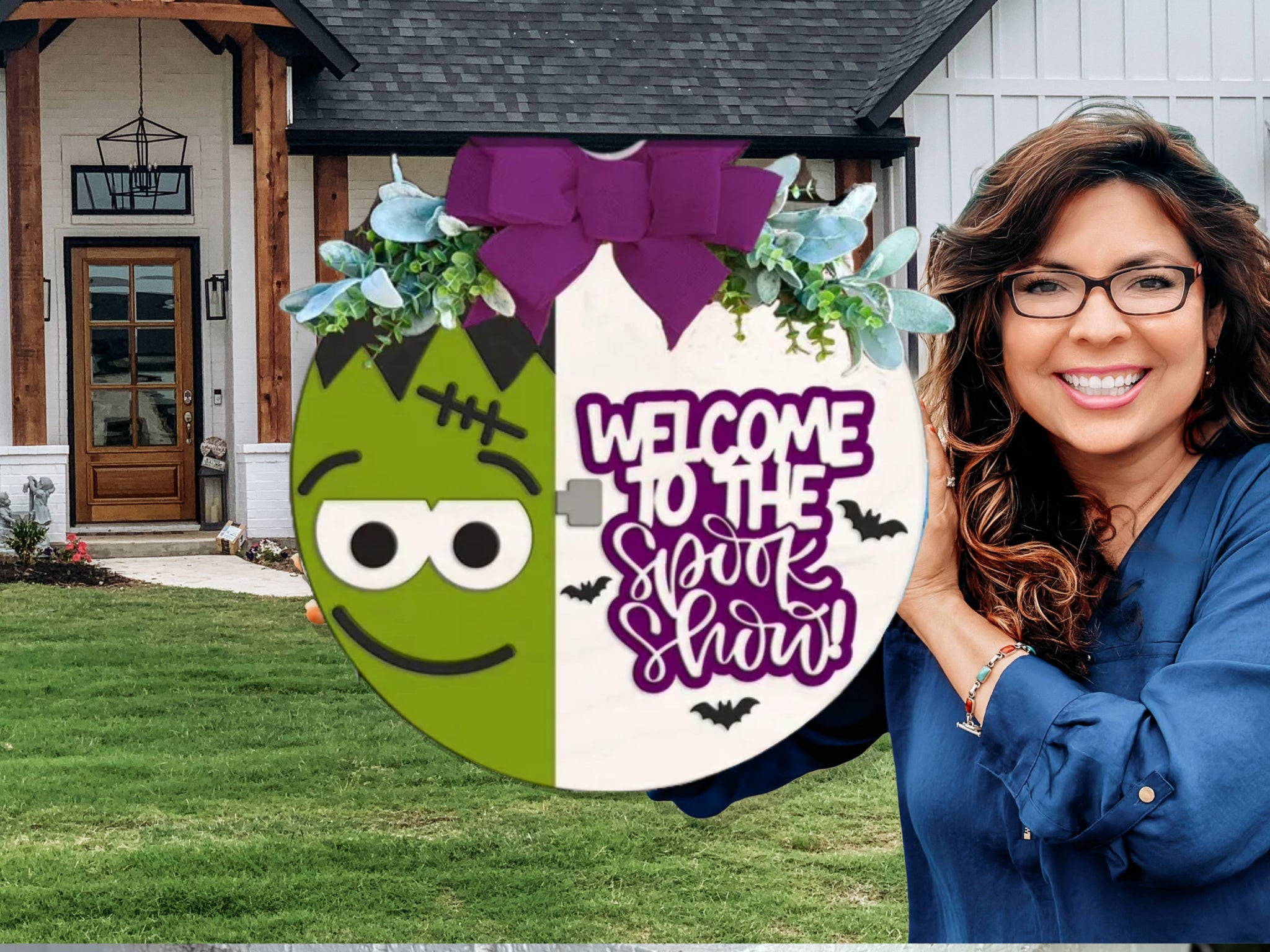 A smiling woman stands outside a house holding a round, festive sign featuring a cartoon Frankenstein face and the text Welcome to the Spook Show with bats, topped with a purple bow and greenery.