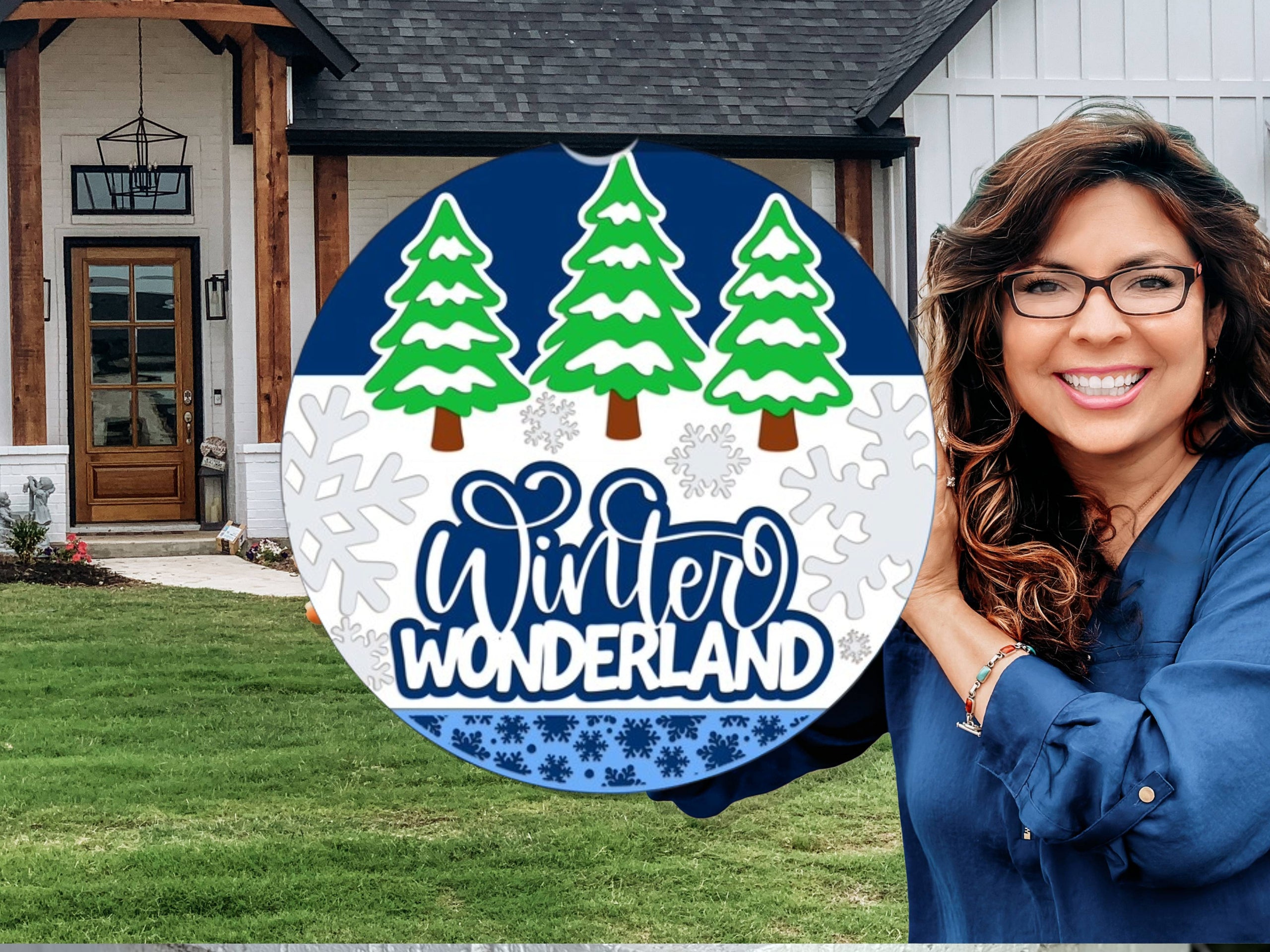 A smiling woman stands in front of a house holding a round sign with three green pine trees, snowflakes, and the words Winter Wonderland in blue and white.