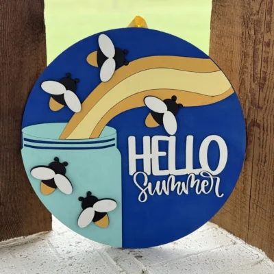 A round sign with a blue background shows lemonade being poured into a glass, surrounded by cartoon bees. The words HELLO summer are written in white cursive and block letters at the bottom right.